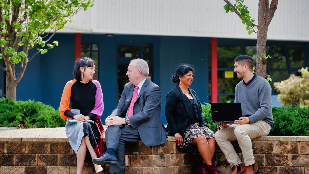 Group of 4 adults sitting outside talking in pairs. 