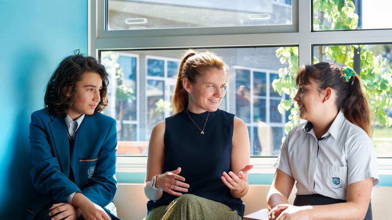 Teacher sitting between two students talking. 