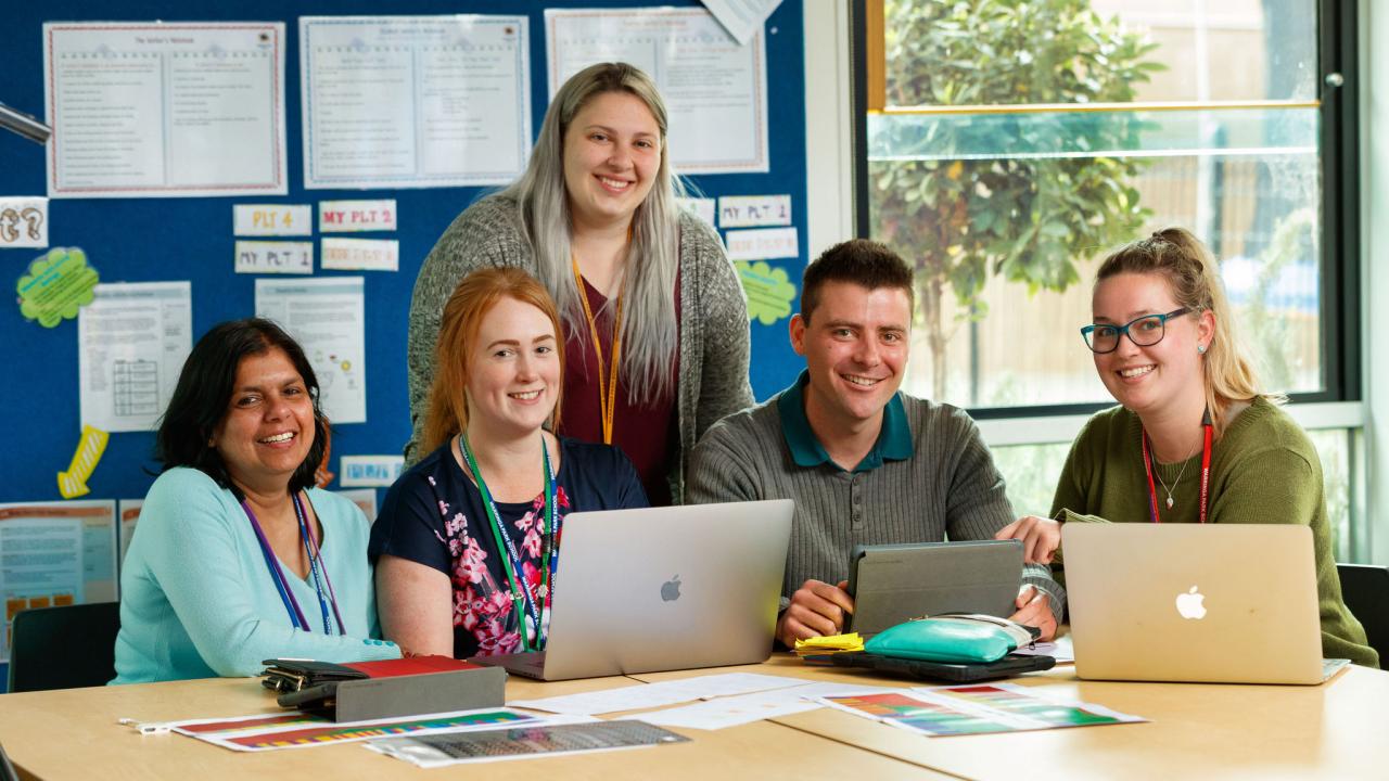 Five adults sitting in front of their laptops at a desk. 