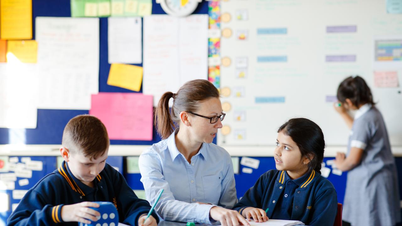 Teacher sitting between two students at desk. 