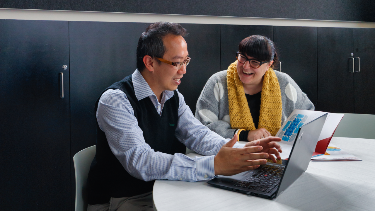 Adults sitting around a table looking at laptop. 