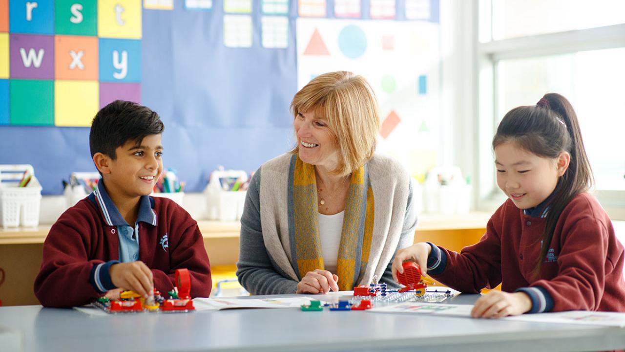 Female teacher seated with primary students at desk