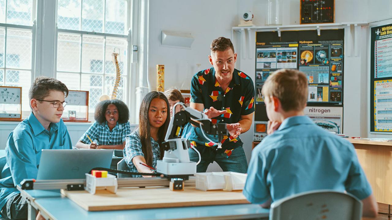 Teacher speaking to high school students at desk in classroom