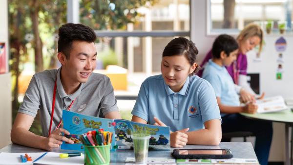 Male teacher sitting with student reading a book. 