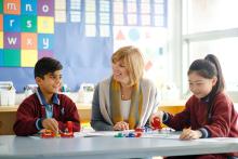 Female teacher seated with primary students at desk