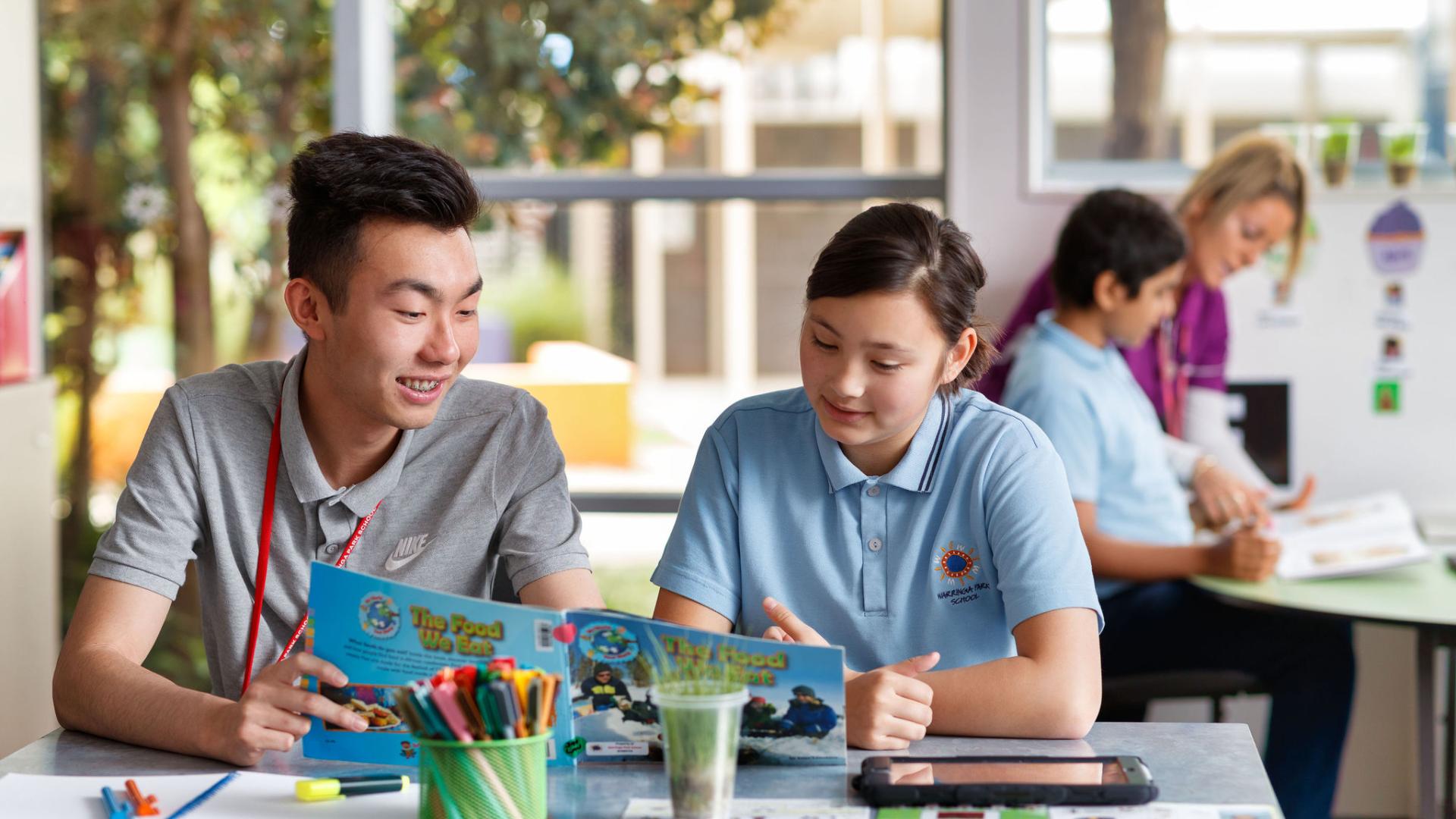 Male teacher sitting with student reading a book. 