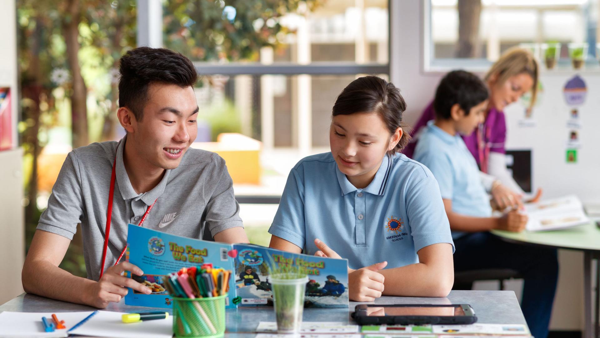 Male teacher sitting with student reading a book. 